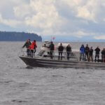 Group of people standing on the deck of covered boat watching wildlife