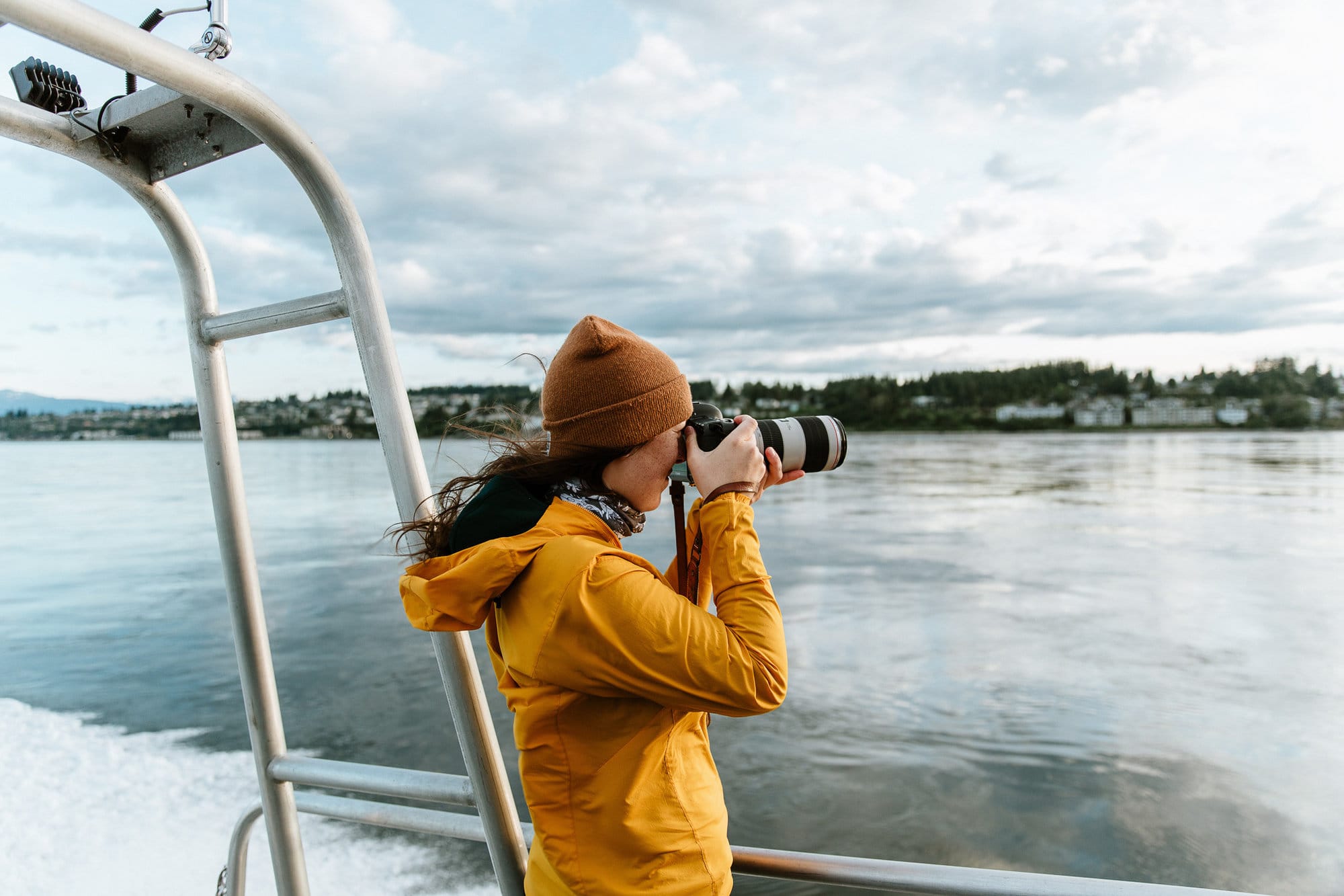 Woman in yellow jacket taking photo from deck of boat
