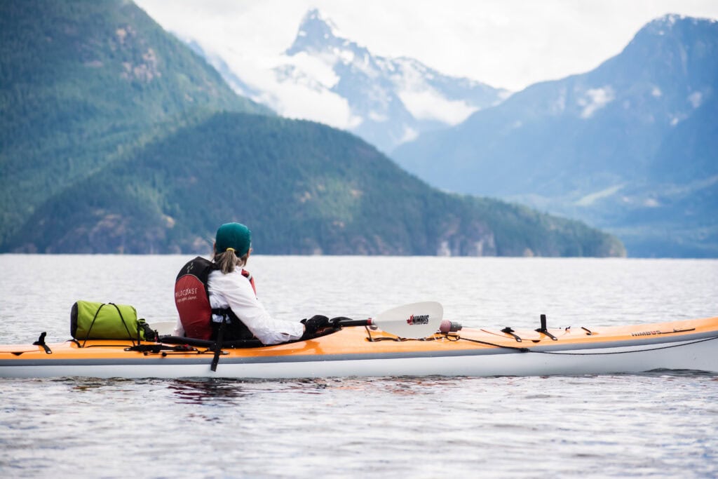 A person is kayaking in the ocean with an orange kayak