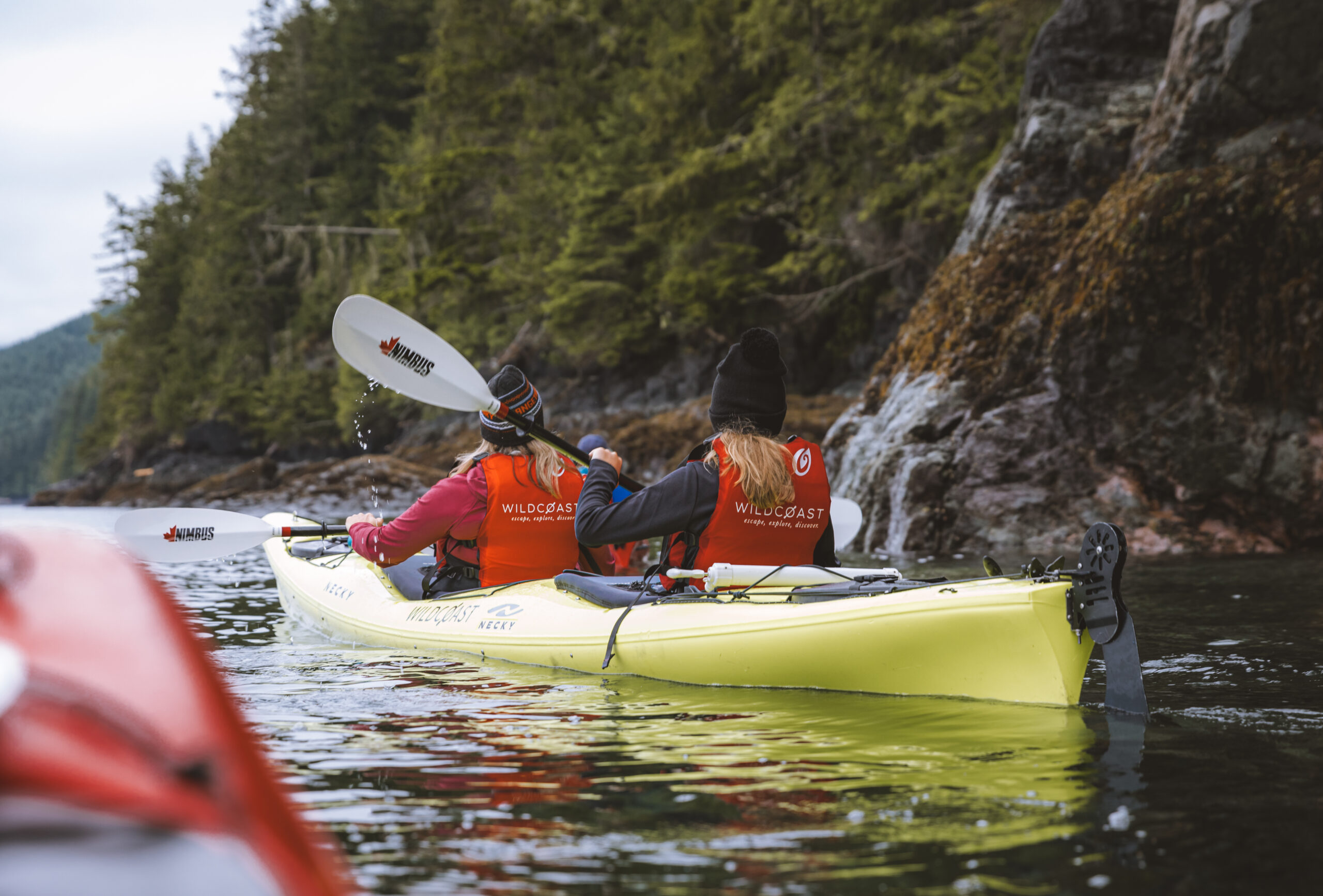 two persons kayaking along the shoreline in a yellow kayak