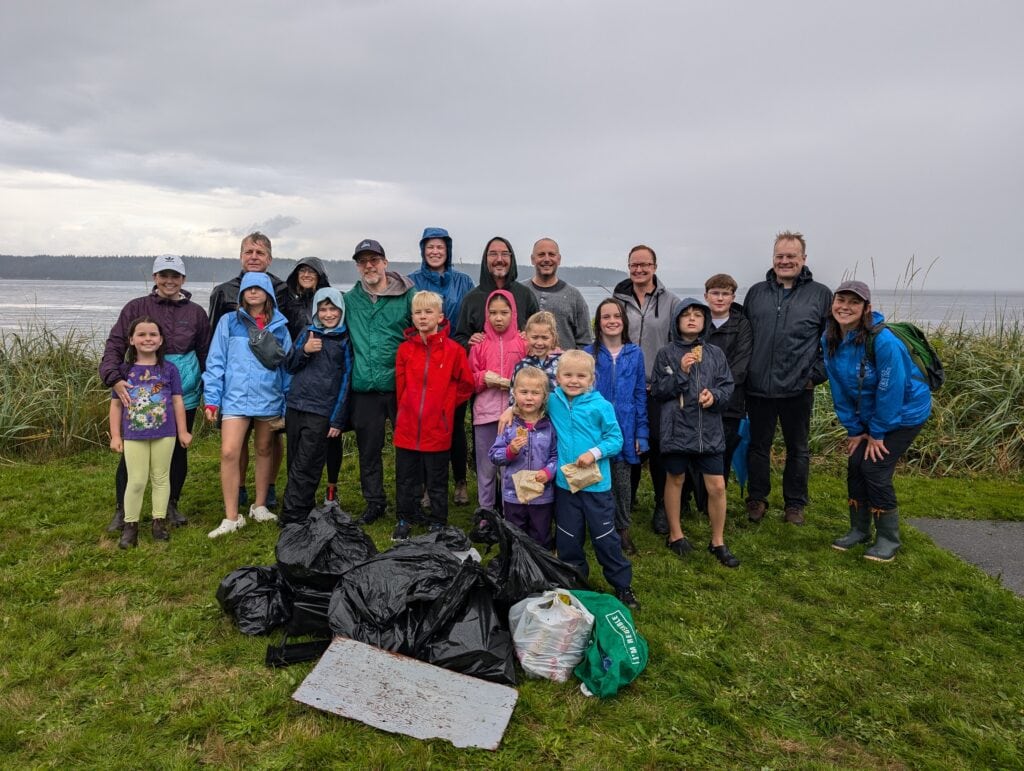 A group of kids and parents standing in front of a beach, showcasing all the garbage they collected during a beach clean up