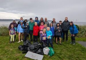 A group of kids and parents standing in front of a beach, showcasing all the garbage they collected during a beach clean up